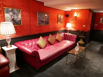 102 Massage Bangkok: red tufted sofa beneath framed pictures and lamps